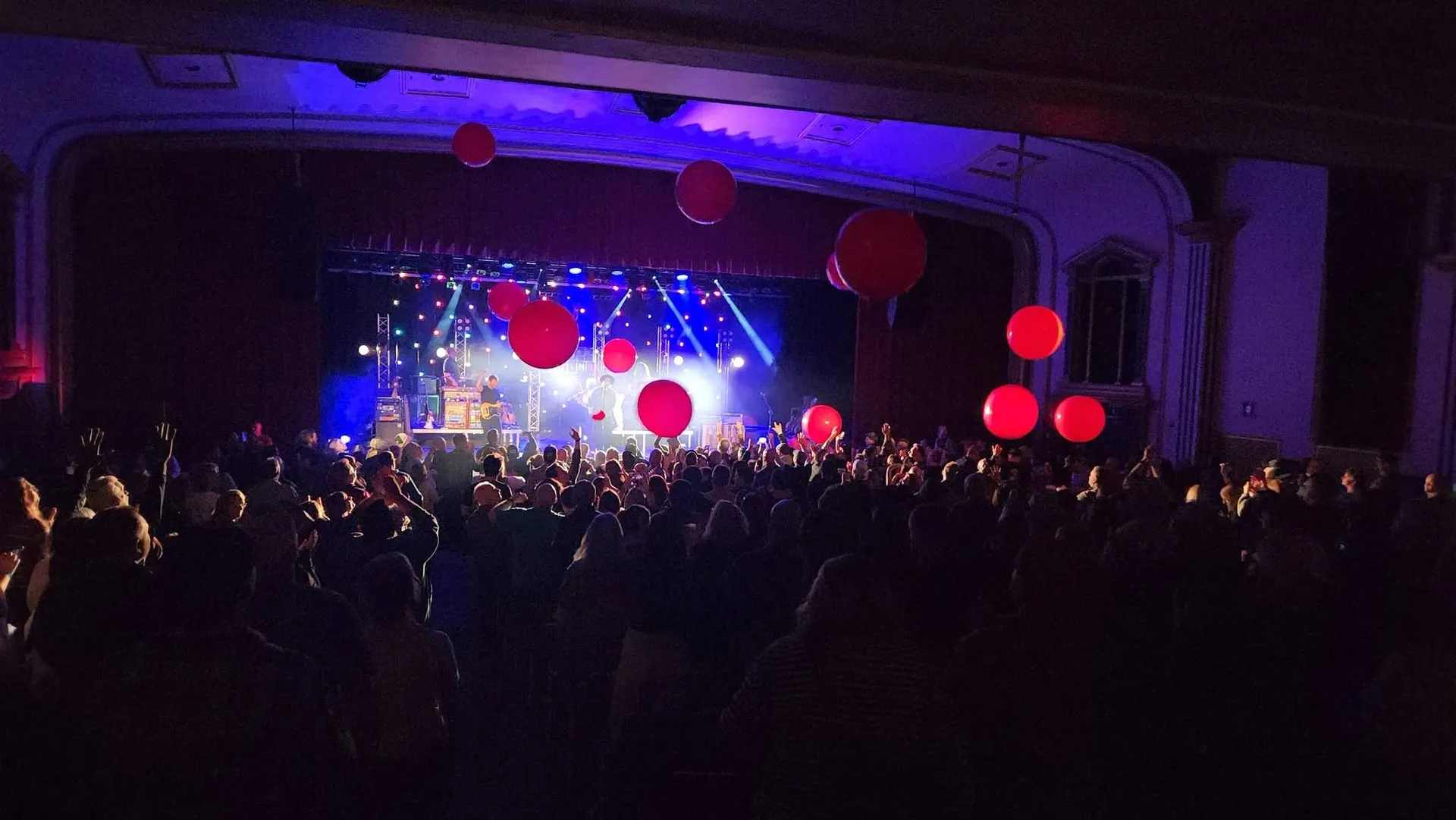 A standing crowd under the proscenium with giant red balloons in the air