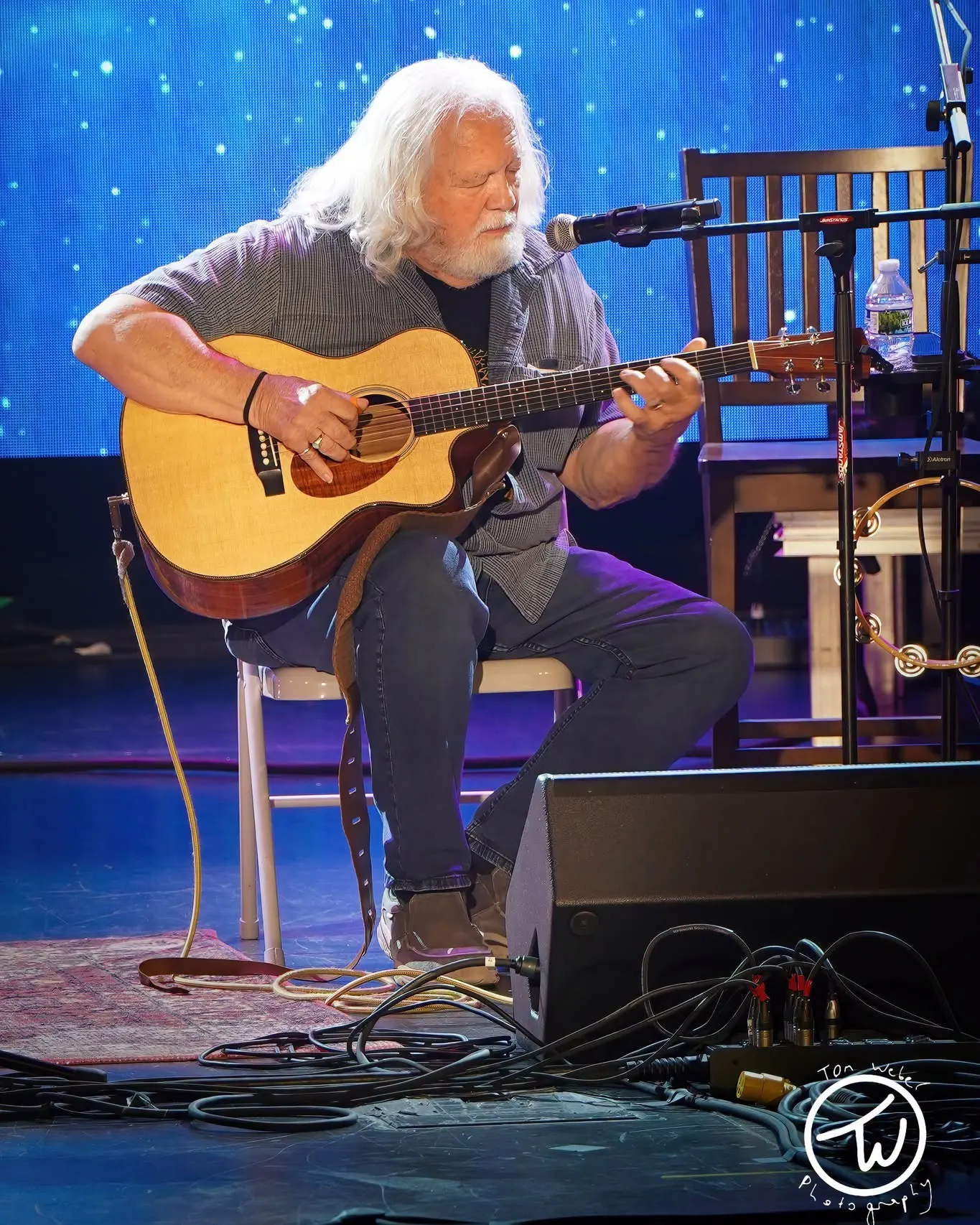 Acoustic guitarist seated, starfield LED wall, vertical crop